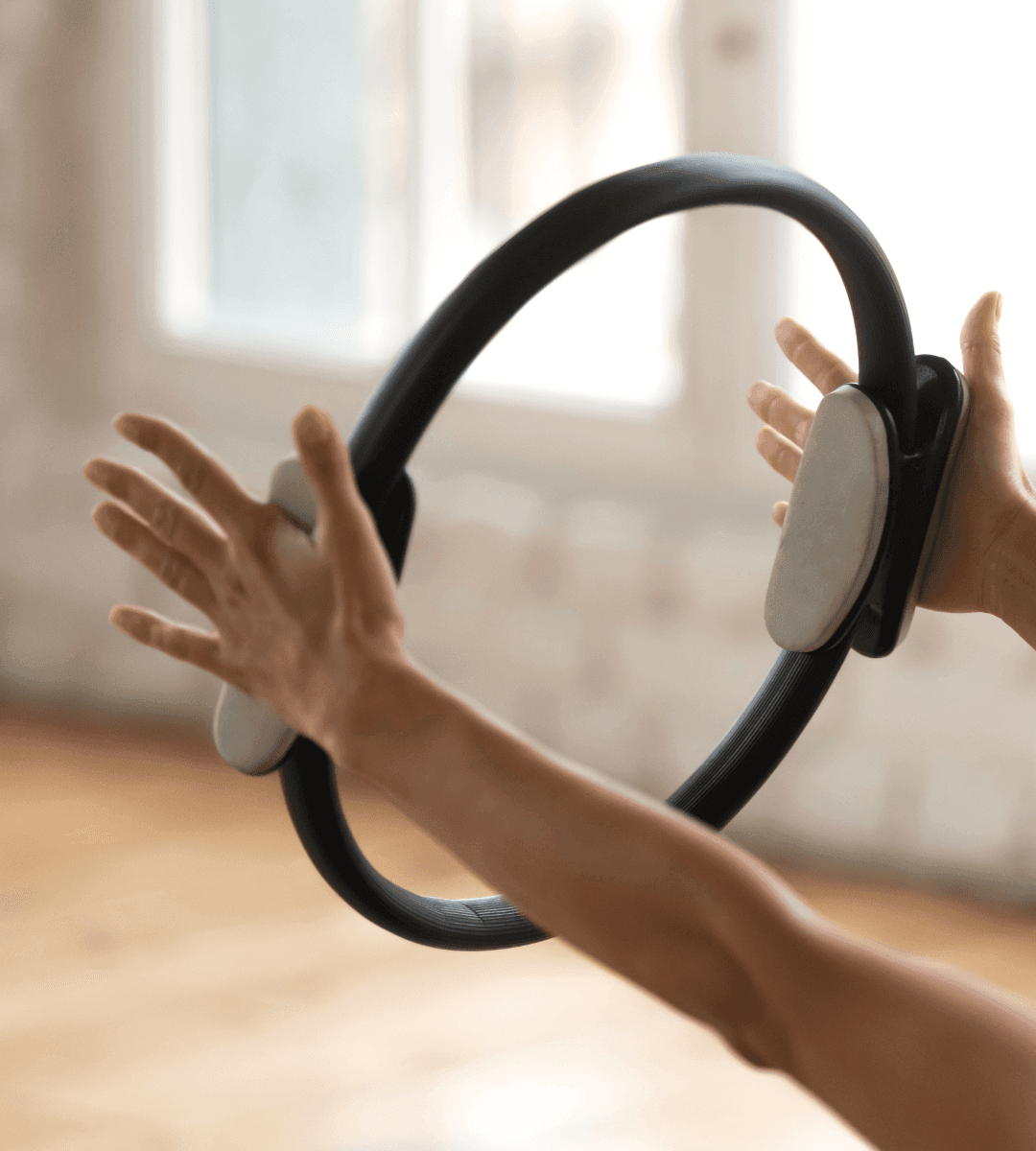 Person holding a pilates ring with both hands during a workout in a bright room.